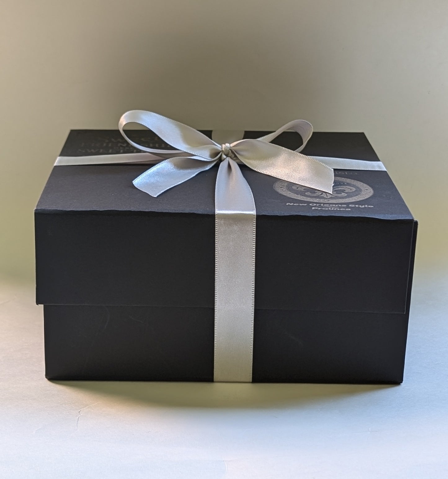 A black gift box with an ivory ribbon bow on top containing pralines